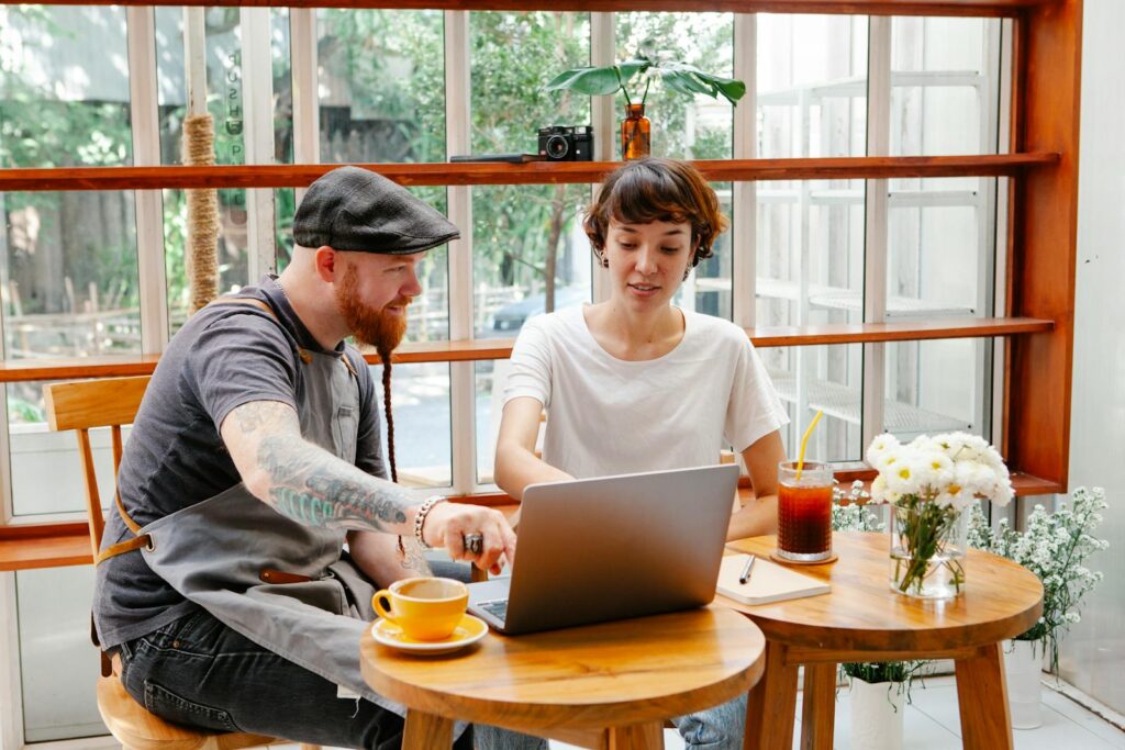 Beyond the Basics: Level Up Your Local SEO with Google Business Profile Attributes Couple of colleagues in aprons and casual clothes in cafe working on laptop at table with glass of drink and coffee cup in daylight